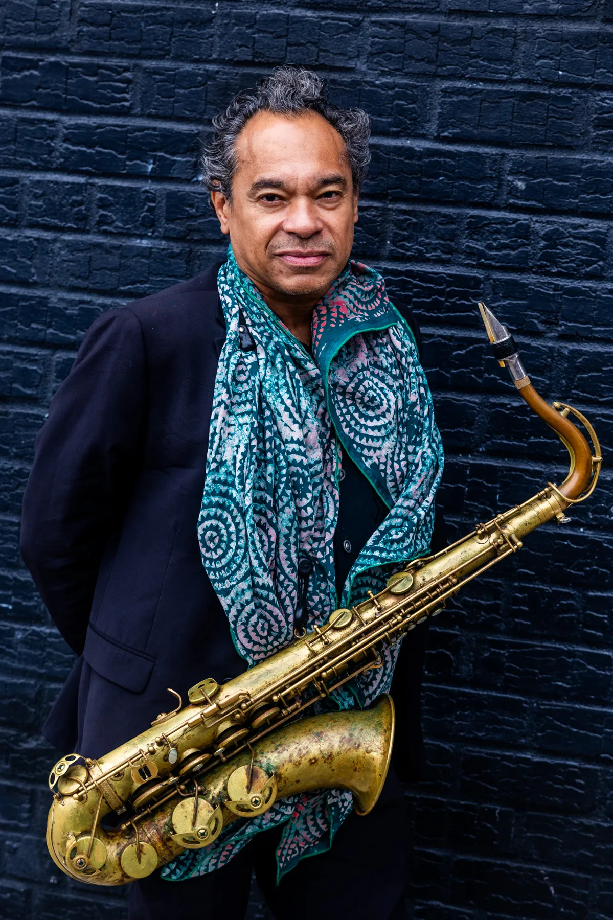 Jay Rodriguez Sierra with saxophone against a brick wall.